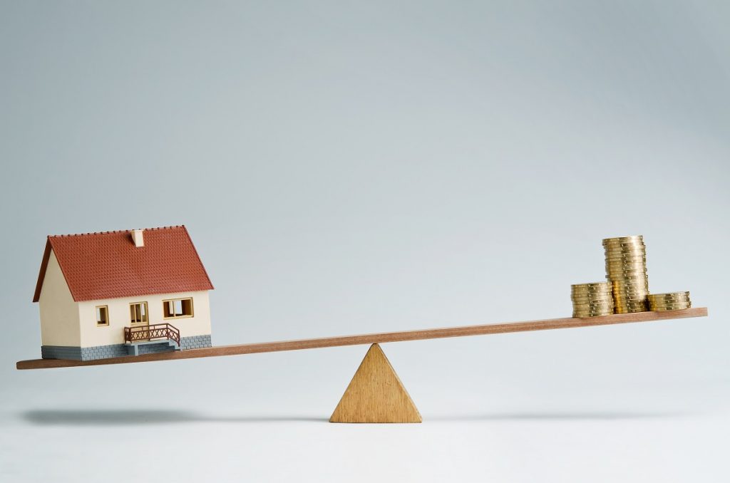 house model and coins balancing on a seesaw